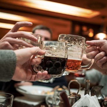 Friends toasting with glass mugs of beer in a warm, lively pub atmosphere.